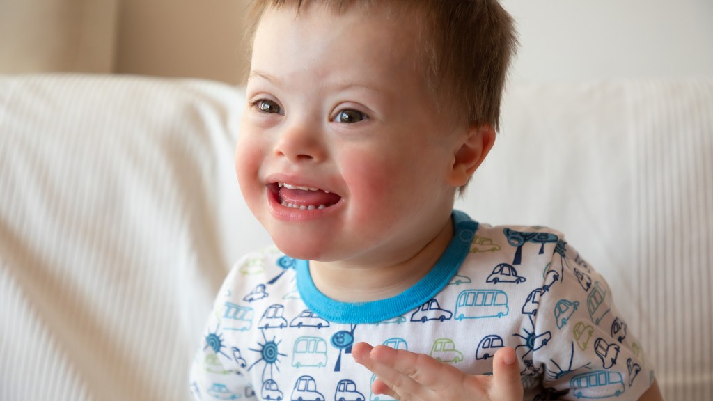 A young boy with Down syndrome smiling warmly while sitting on a light-colored sofa