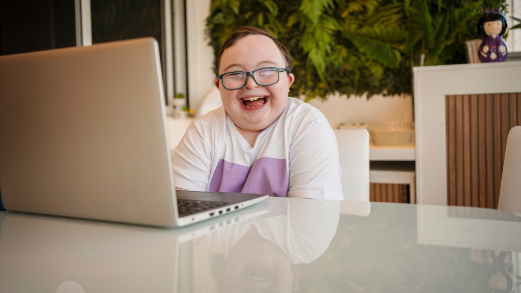 A teenage boy with Down syndrome laughing while working on a laptop at a bright table