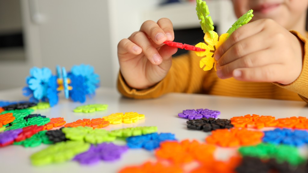 A child's hands connecting colorful flower-shaped interlocking building blocks on a white table