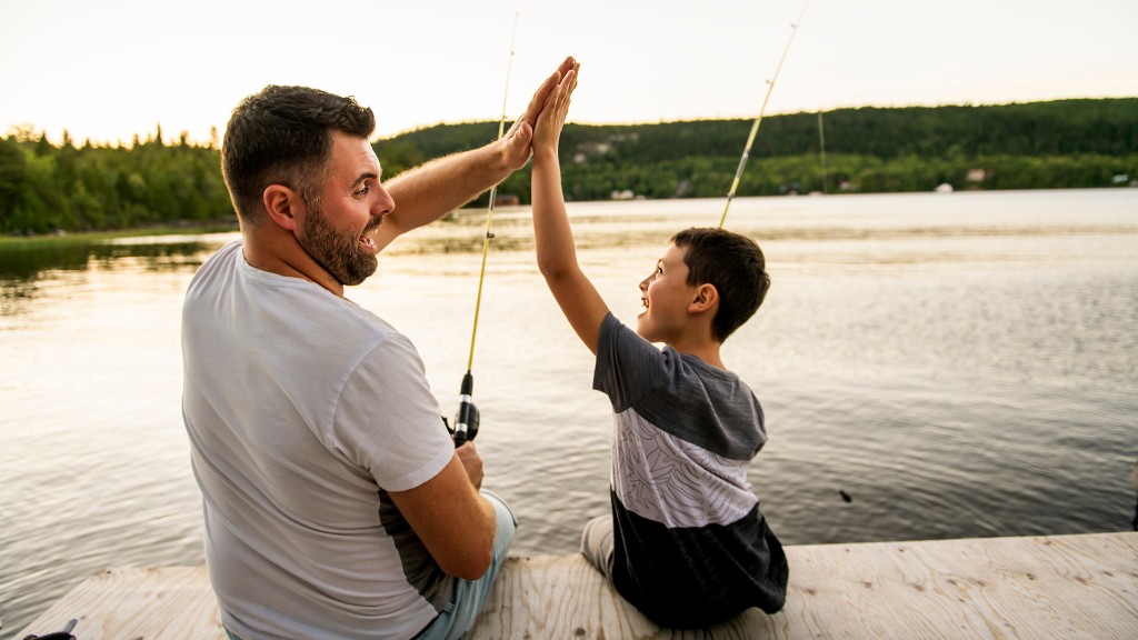 A father and son high-fiving while fishing together on a wooden dock at sunset