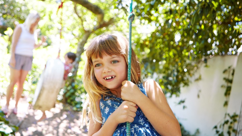 A smiling young girl holding a blue rope swing outdoors in a sunny backyard