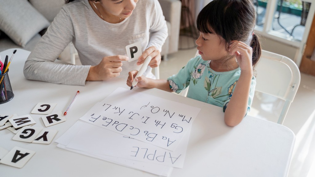 A woman holding a letter P flashcard while a young girl practices writing the alphabet at a table