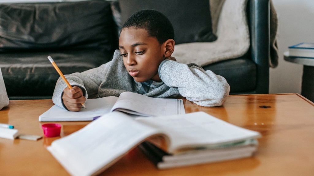 A boy leaning on his hand while writing in a notebook at a wooden table at home