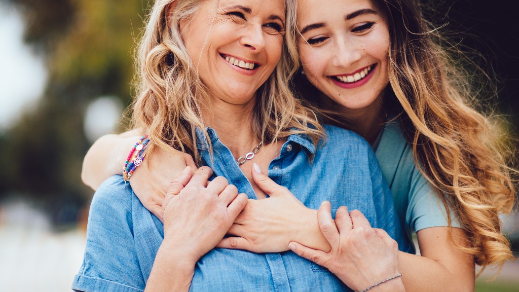 A mother and teenage daughter hugging outdoors in warm sunlight, both smiling with eyes closed