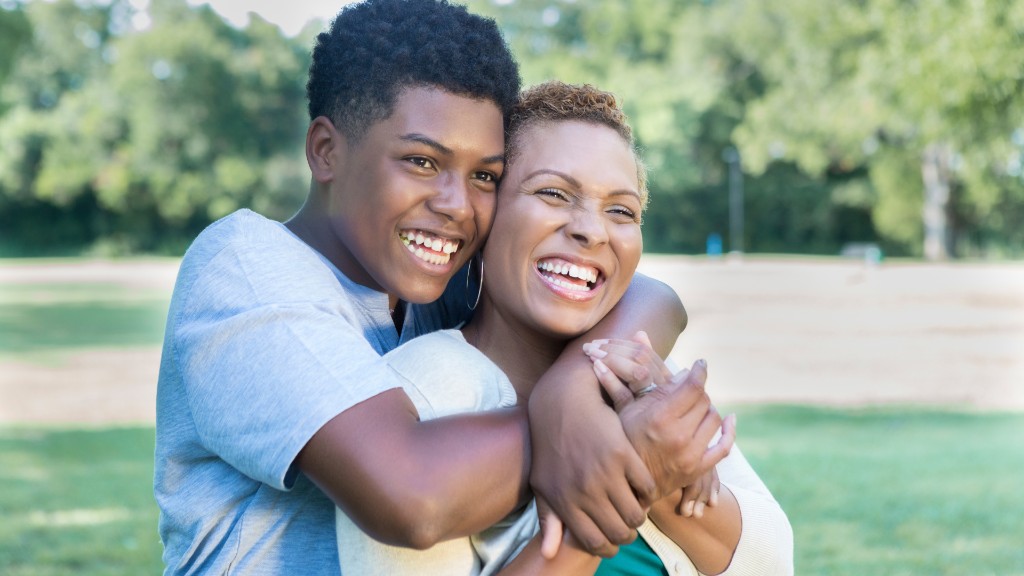 A mother and teenage son laughing and hugging outdoors in a sunny park
