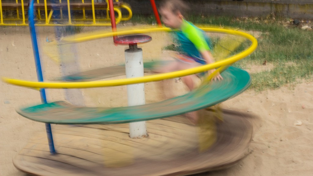A motion-blurred photograph of a child spinning rapidly on a playground merry-go-round