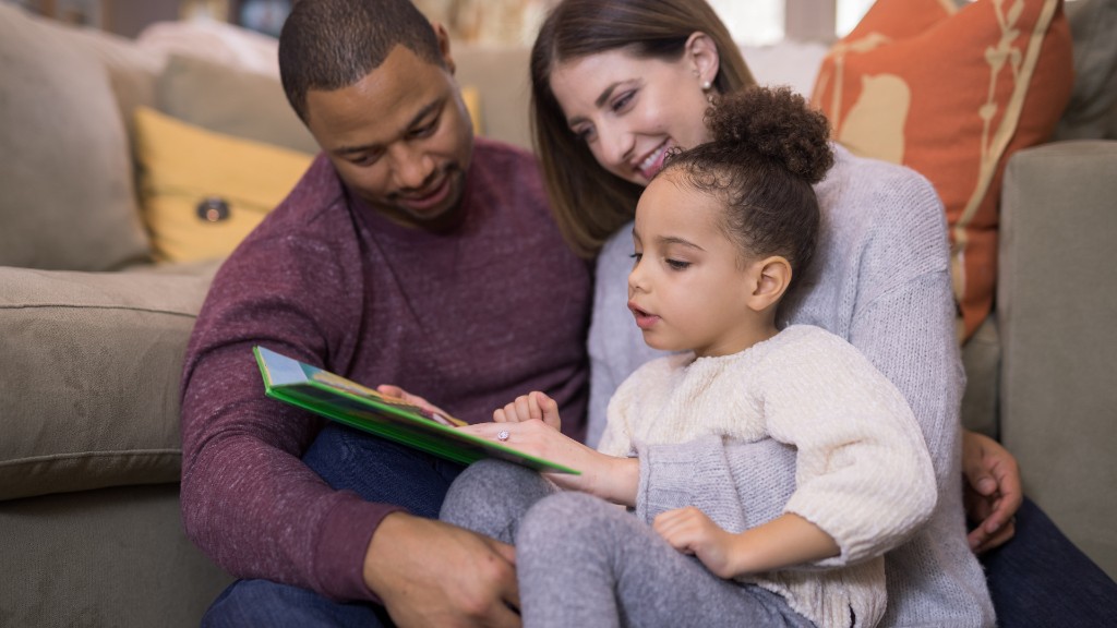 A mother, father, and young daughter reading a picture book together on the floor in a warm living room