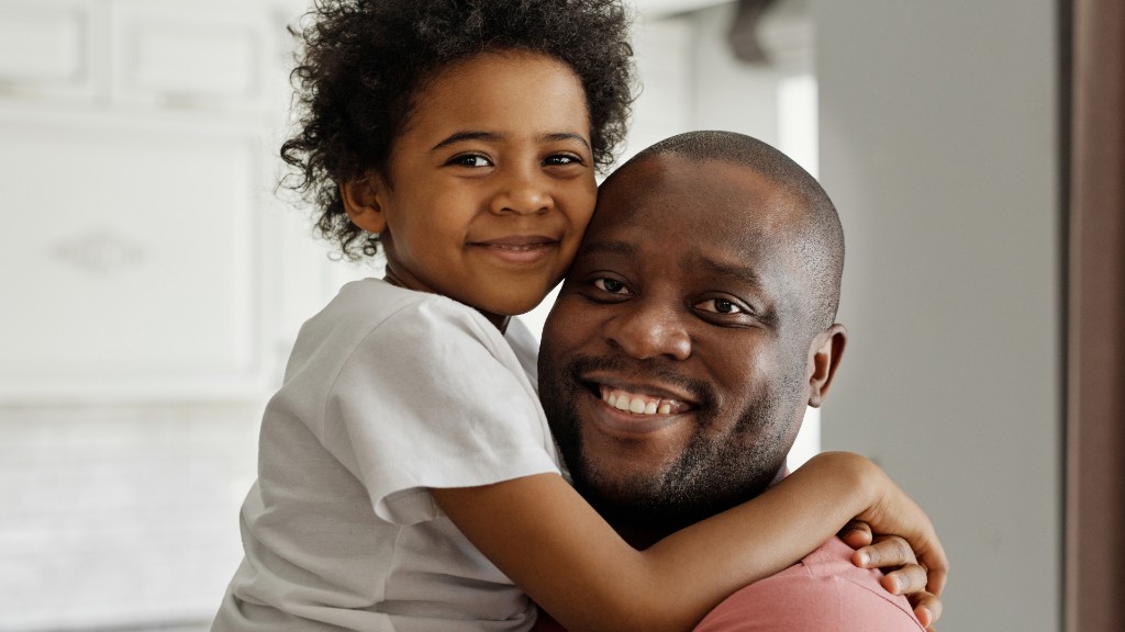 A smiling father with his young son hugging him from behind in a bright home