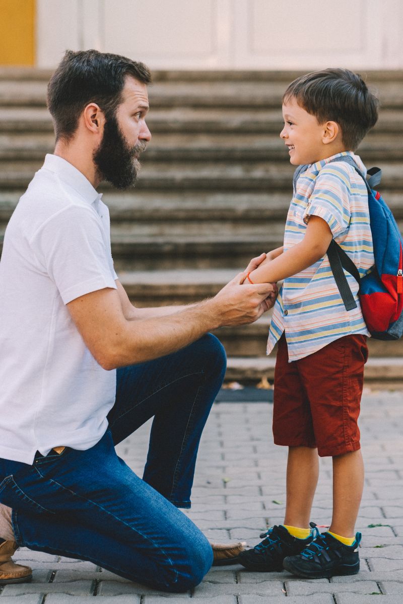 A father crouching at eye level with his child on a school walkway