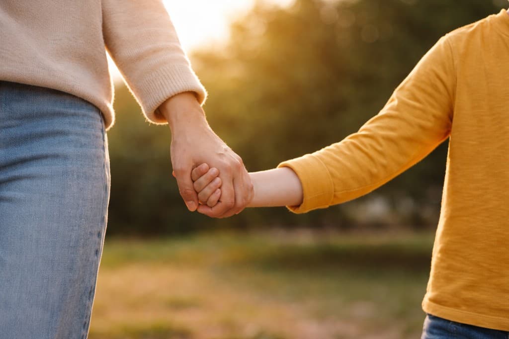 Parent and child holding hands outdoors in warm sunlight